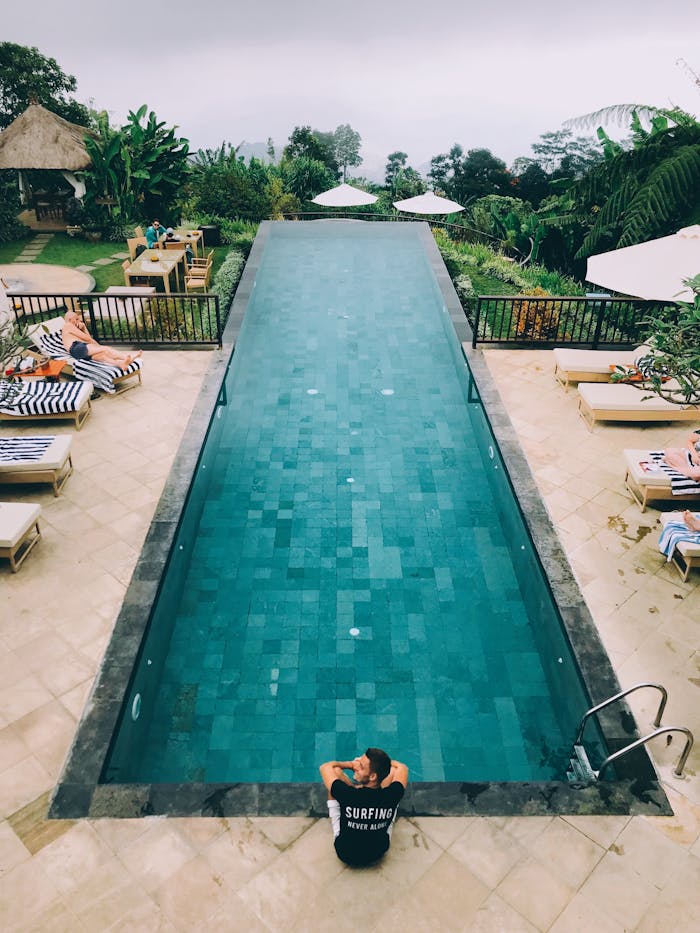 Man in Black Shirt Sitting beside the Swimming Pool